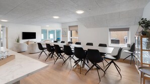 Ein Konferenzraum mit langem Tisch, schwarzen Stühlen, einem Fernseher und einer Pflanze.