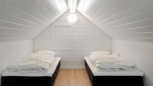Ein kleiner Raum mit weißen Wandverkleidungen, zwei Betten, Holzboden und einer zentralen Leuchte.