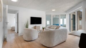 Ein modernes Wohnzimmer mit Flachbildfernseher, zwei runden Sesseln, einem kleinen Tisch und einer Topfpflanze.