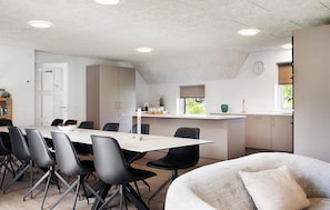 Eine moderne Küche mit einer großen Kochinsel, einem Essbereich mit einem langen Tisch und Stühlen sowie einer gemütlichen Sitzecke mit einer Couch.