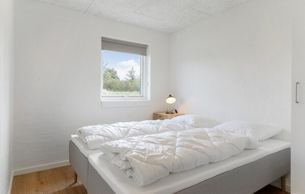 A bedroom with a bed, a window, and a bedside table with a lamp.