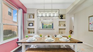 Een eetruimte met een houten tafel voor vier personen, een hanglamp en planken met verschillende spullen.