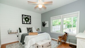 A bedroom with a bed, a window, a dog, and a ceiling fan. - Adirondack Fall Haven: Hot Tub, Fireplace, Coffee Bar, Dogs Welcome! (Upper Jay)
