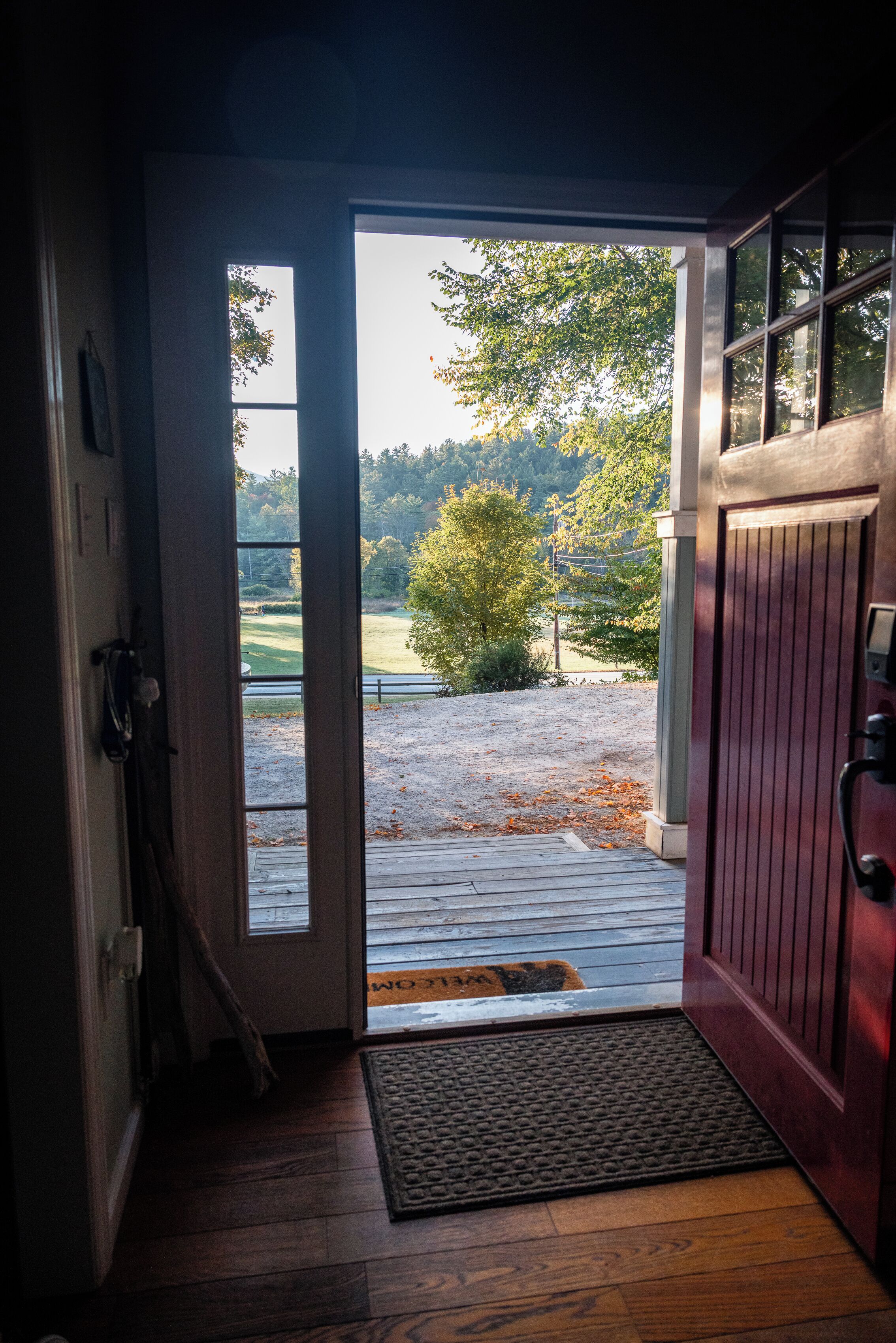 Une porte ouverte donnant sur un espace extérieur abrité, avec vue sur des arbres et un champ d’herbe.