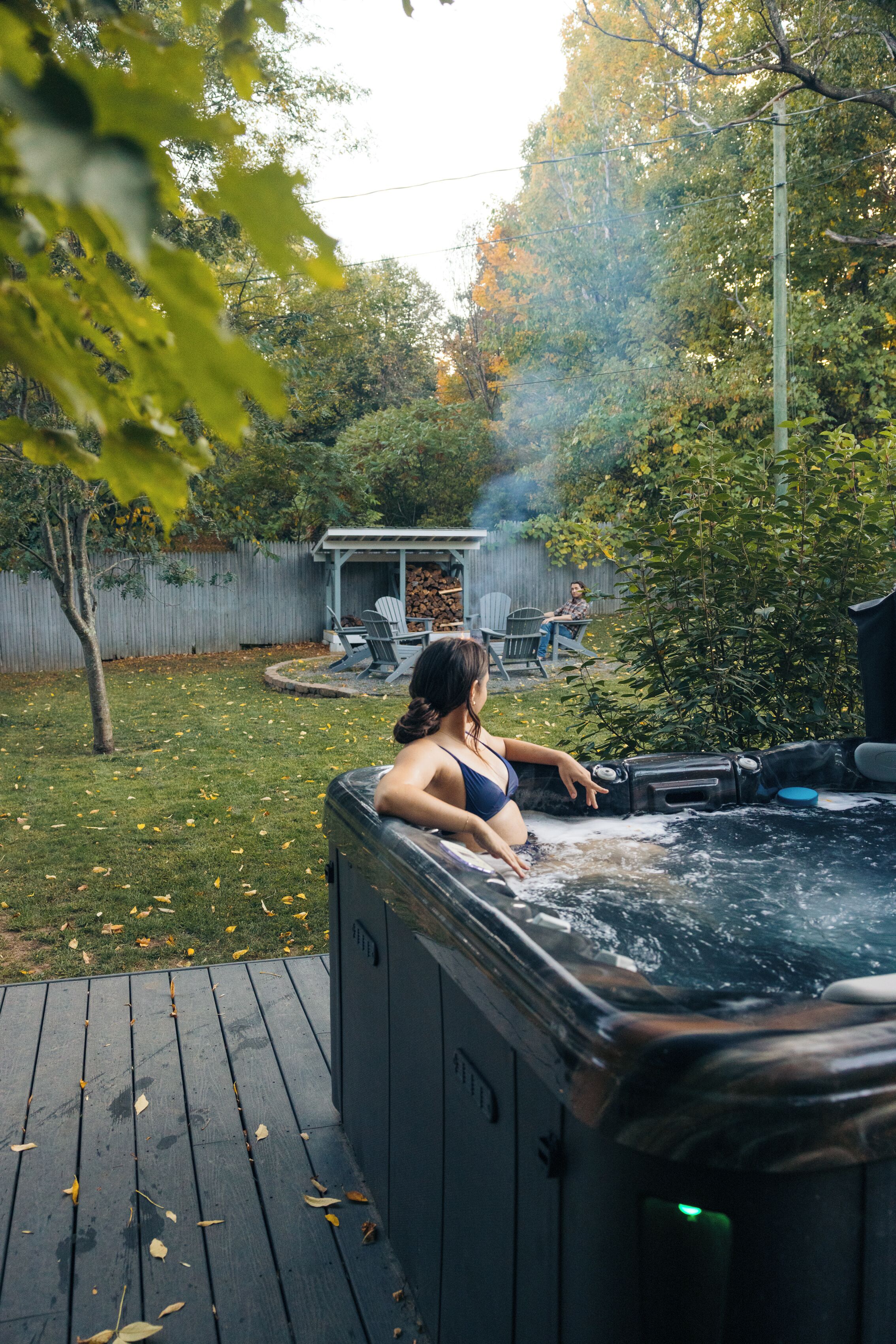 A hot tub on a wooden deck with a grassy yard and a wooden fence in the background.