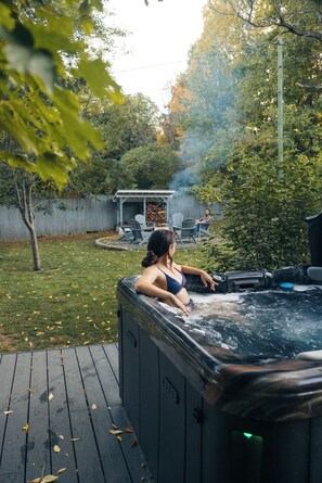 Ein Whirlpool auf einer Holzterrasse mit einem Rasen und einem Holzzaun im Hintergrund.