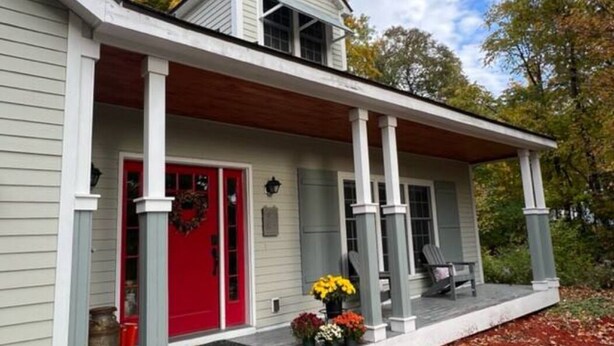 A house with a red door, a porch with a bench, and a small garden with flowers. - Adirondack Fall Haven: Hot Tub, Fireplace, Coffee Bar, Dogs Welcome! (Upper Jay)