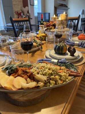 Une table à manger dressée avec différents plats, dont un grand plat de service rempli de nourriture, des verres à vin et des éléments décoratifs.