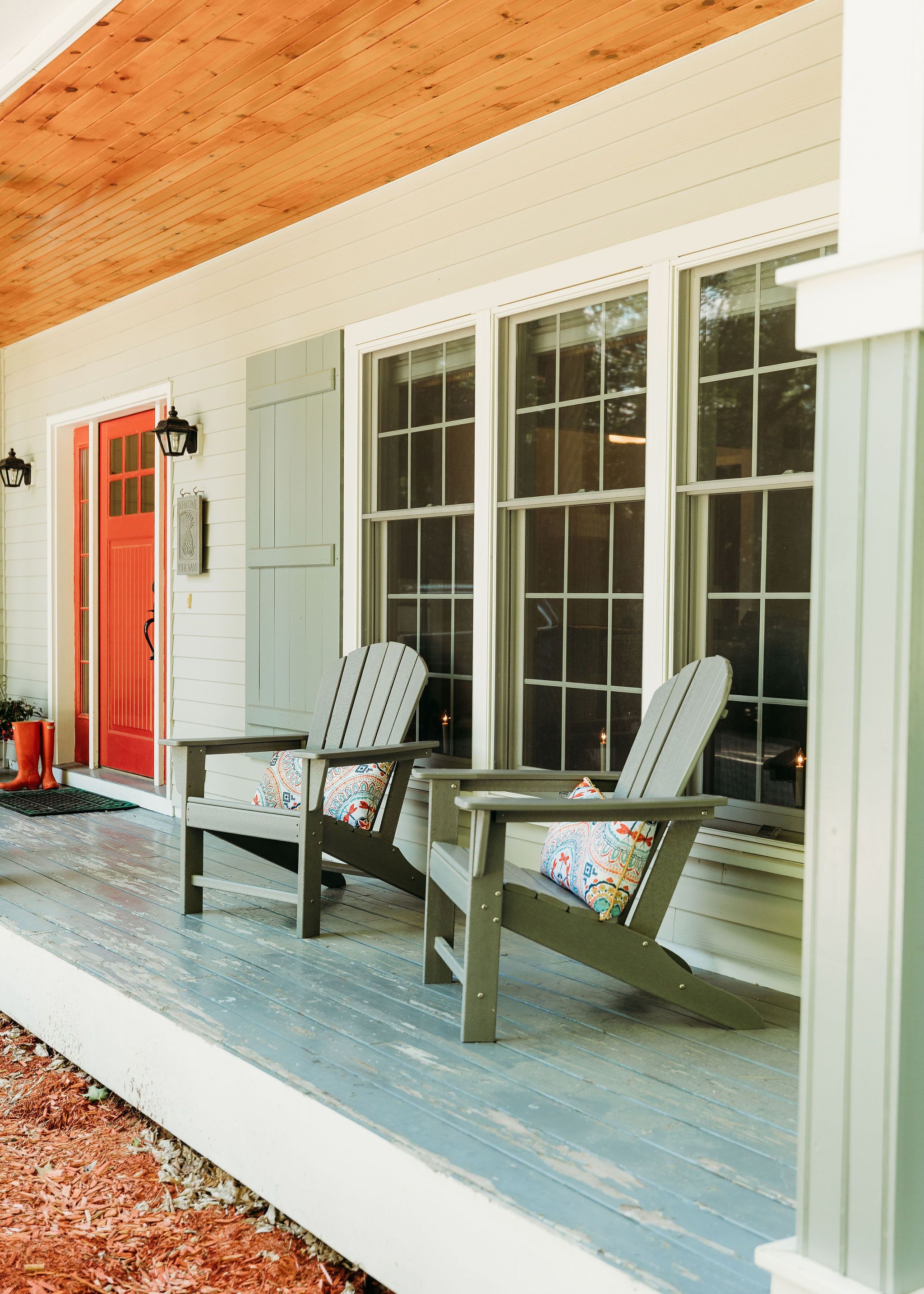 Une véranda avec deux fauteuils Adirondack et une porte rouge.
