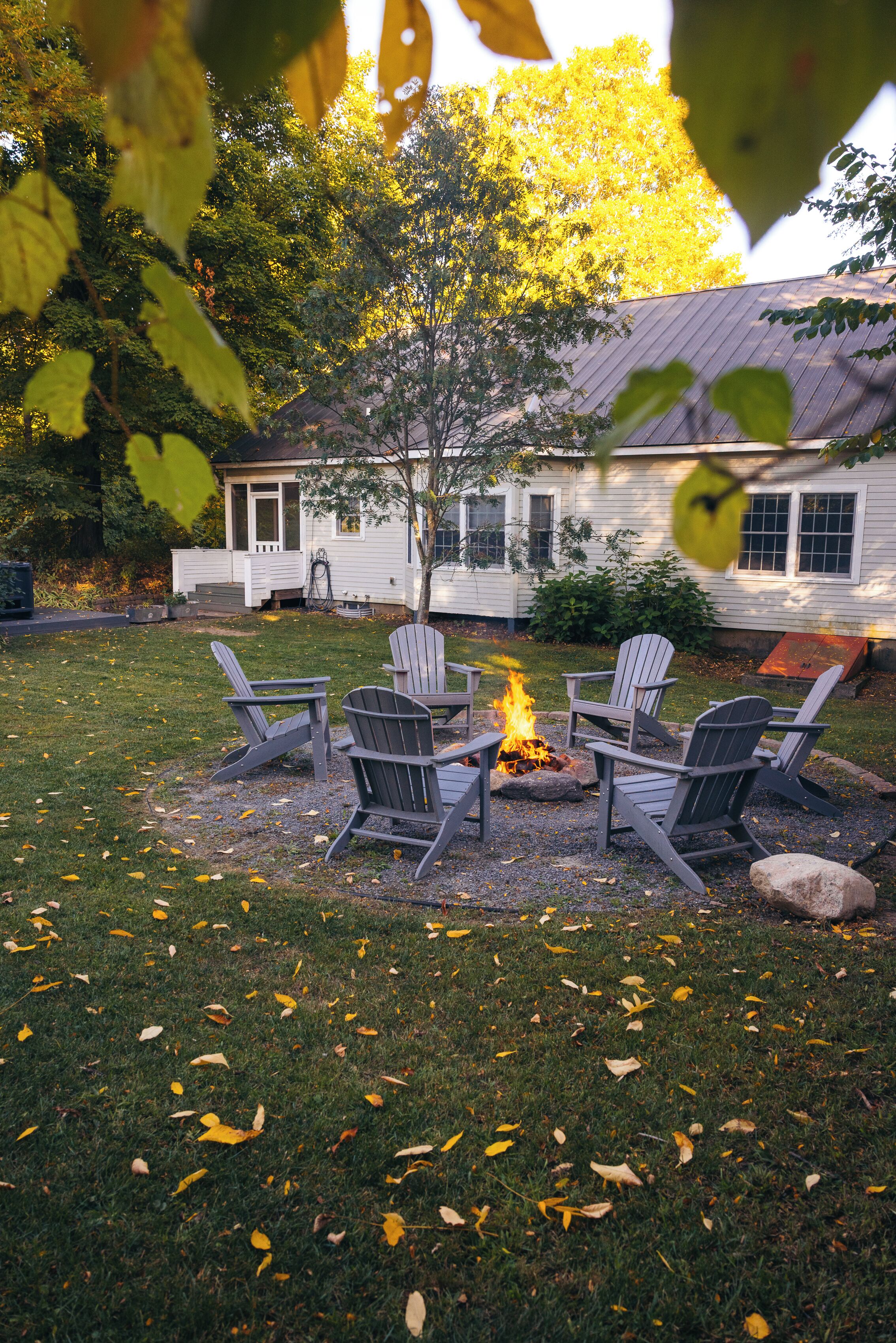 A backyard with a fire pit and Adirondack chairs.