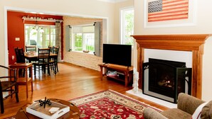 A living room with a fireplace, a television, and a dining area with chairs and a table. - Adirondack Fall Haven: Hot Tub, Fireplace, Coffee Bar, Dogs Welcome! (Upper Jay)