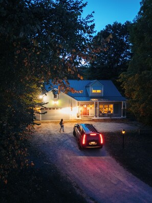 Une maison avec une allée, une voiture et une personne debout près de l’entrée.