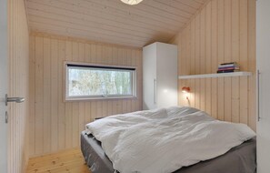 Makuuhuone, jossa on puinen katto, ikkuna, sänky, vaatekaappi ja hylly kirjoja varten.