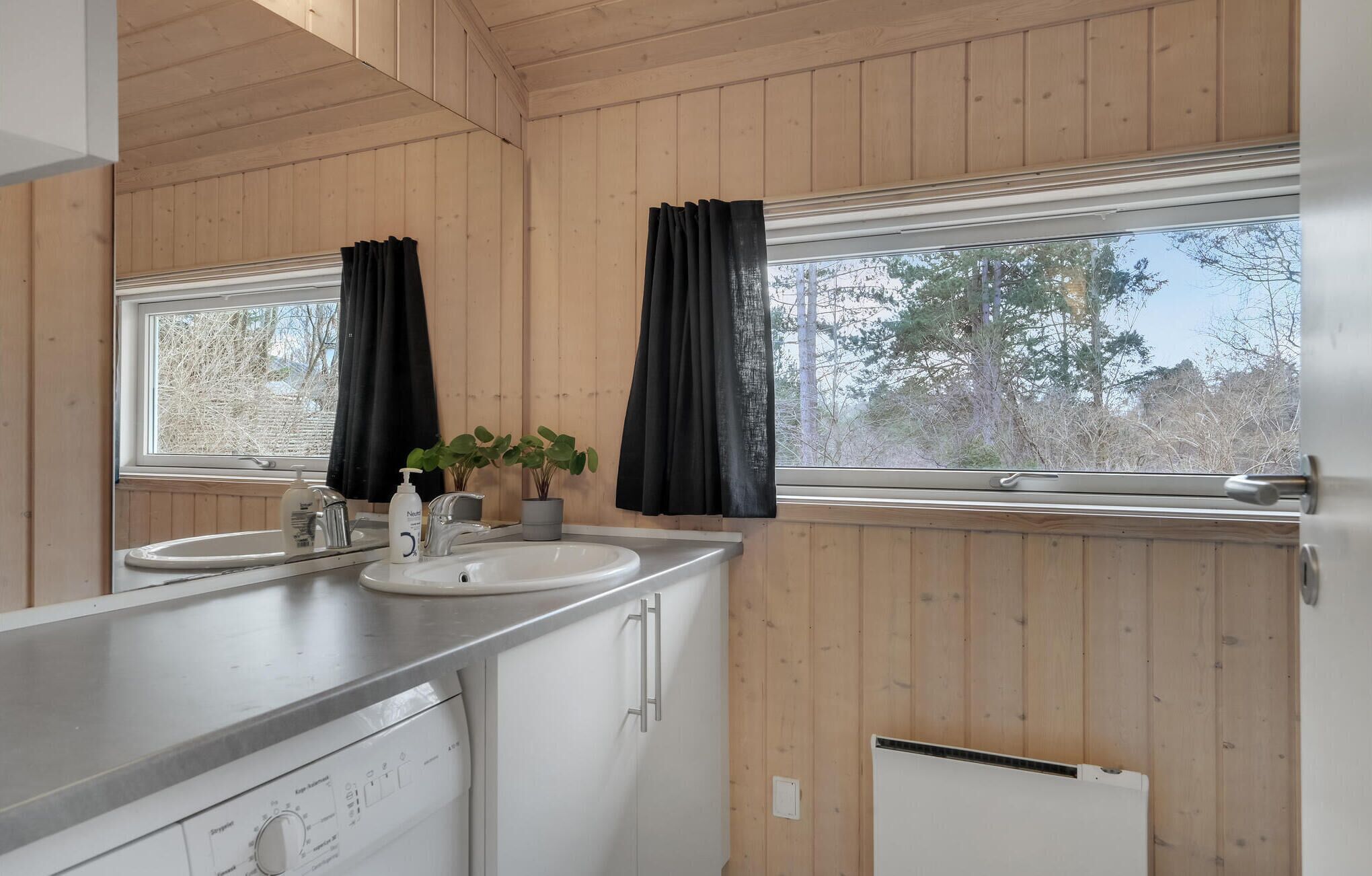 A wooden-paneled bathroom with two sinks, a mirror, and a window with black curtains.