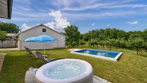 Un patio trasero con jacuzzi, piscina y un área de patio techada.