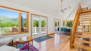 A spacious room with large windows, a wooden staircase, and a view of green hills. - Luxury Home with MountainViews•PoolTable•Chefs Kitchen•FirePit (Lake Lure)