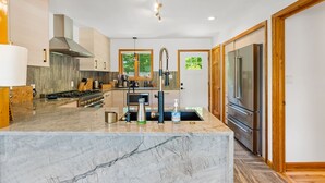 A modern kitchen with a marble island, stainless steel appliances, and wooden cabinetry. - Luxury Home with MountainViews•PoolTable•Chefs Kitchen•FirePit (Lake Lure)