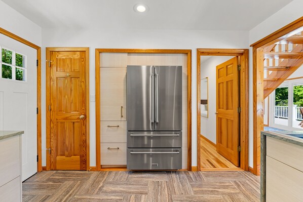 A modern kitchen with a stainless steel refrigerator, wooden doors, and a herringbone-patterned floor.