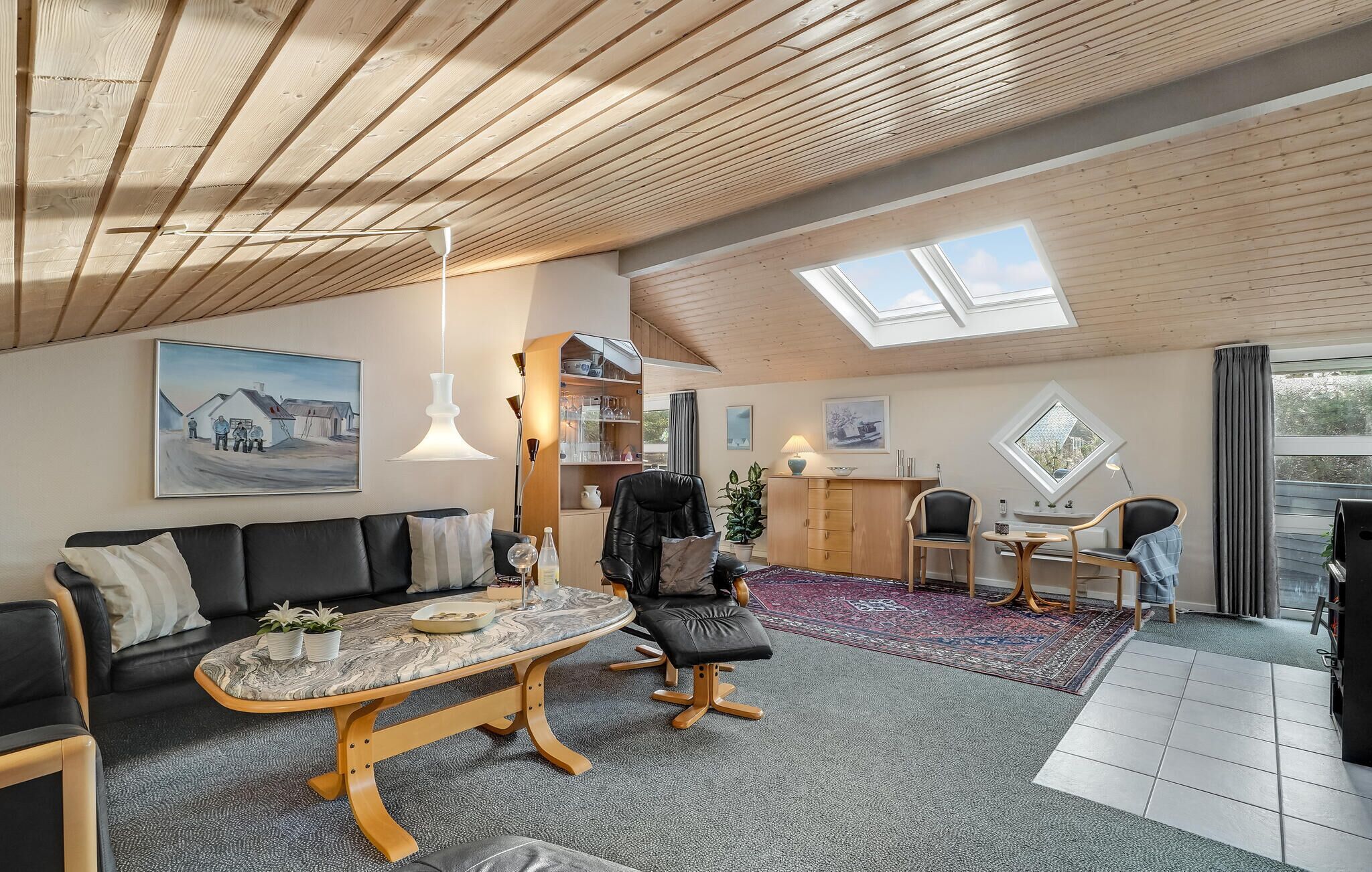 Um amplo loft com pé direito alto, claraboias, uma área de estar aconchegante com sofá e poltronas, uma mesa de jantar e um espaço de cozinha com armário e uma planta.