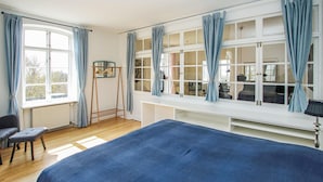 A bedroom with a large bed, a desk, and a chair. There is a window with curtains, a radiator, and a hanging rack with clothes. - Amazing apartment in Samsø with WiFi (Samsø)
