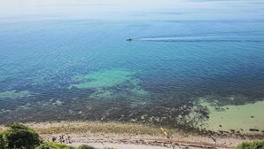 A coastal view with clear water, a boat creating a wake, and a rocky shoreline with people walking. - Amazing apartment in Samsø with WiFi (Samsø)