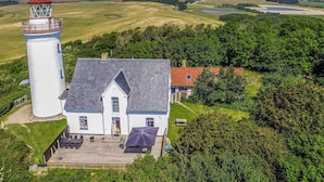 A lighthouse with a white tower and red roof, a white building with a grey roof, and a surrounding landscape with trees and open fields. - Amazing apartment in Samsø with WiFi (Samsø)