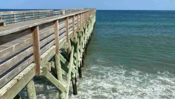 Une jetée en bois s’avançant dans la mer, avec une eau claire et de douces vagues.