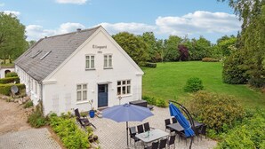 Een wit gebouw genaamd 'Ellegard 1855' met een geplaveid terras, zitplaatsen buiten en een tuin.