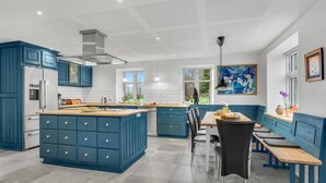 Een moderne keuken met blauwe kastjes, een centraal eiland en een zithoek met een bank.