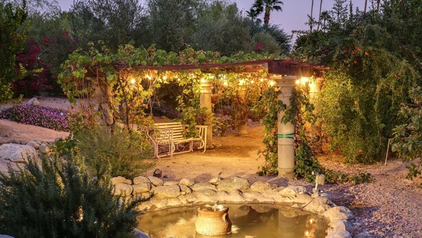 Un giardino con uno stagno, una panchina in legno e un pergolato con luci a stringa.