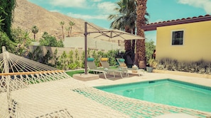 Un espace piscine aménagé avec des chaises longues, un hamac et une pergola offrant de l’ombre.