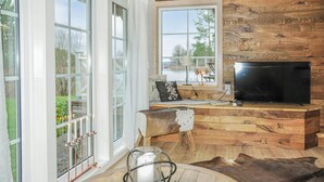 Un salon chaleureux avec une grande télévision, des lambris en bois, un banc et une vue sur un paysage enneigé par les fenêtres.