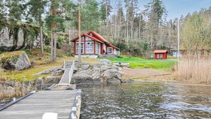 Une cabane avec un quai s’avançant dans un lac, entourée d’arbres et d’une petite construction rouge située à proximité.