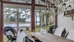 Un espace extérieur abrité, aménagé avec des sièges, et offrant une vue sur un lac et des arbres.