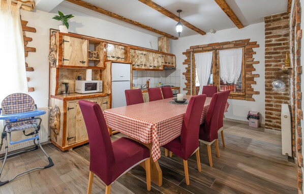 A cozy kitchen with wooden cabinets, a microwave, and a dining area with a checkered tablecloth and red chairs.