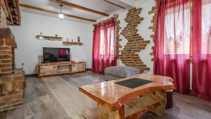 Una sala de estar con una mesa de centro de madera, un televisor sobre un mueble de madera, cortinas rojas y una pared de ladrillo.