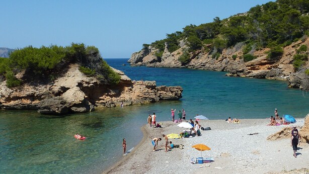 A beach with rocky terrain, clear water, and people sunbathing. - Villa Bachata with private pool Bonaire (Alcúdia)