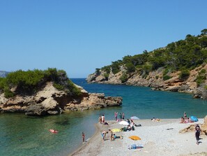 Ein Strand mit felsigem Gelände, klarem Wasser und Personen, die sich sonnen.