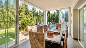 A dining area with a large table, wicker chairs, and a view of a swimming pool and greenery outside. - Villa Bachata with private pool Bonaire (Alcúdia)