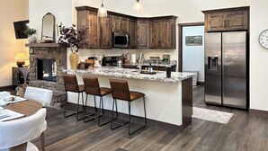 Une cuisine moderne avec des meubles de couleur bois foncé, un réfrigérateur en acier inoxydable, un îlot central en marbre avec des tabourets de bar et une cheminée en pierre.