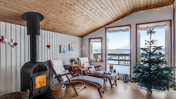 A cozy room with a wood-burning stove, comfortable seating, a small Christmas tree, and large windows offering a view.