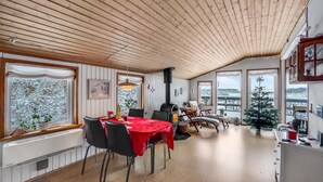 A dining area with a red tablecloth, wooden ceiling, and large windows with snowy views.