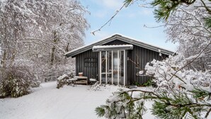 A wooden cabin with a covered porch, surrounded by snow-covered trees and bushes.