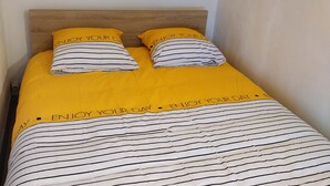 A bed with a striped bedspread and two pillows, one yellow and one striped, in a room with a plain wall and a painting above the bed. - Gien bridge (Gien)