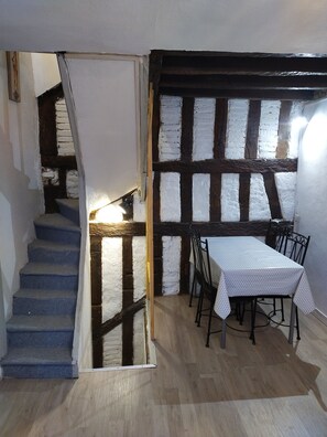 A dining area with a table and chairs, a staircase, and exposed wooden beams.