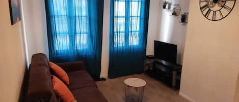 Una sala de estar con un sofá marrón, una mesa de centro redonda y un mueble para televisión.