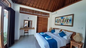 Un dormitorio con techo de madera, cama con ropa de cama azul y blanca, escritorio con silla, armario y un cuadro en la pared.