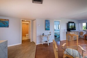 A spacious living area with a wooden floor, a dining table with chairs, a television, and a painting on the wall. - Peekaboo View of Atlantic Ocean - Free Kayaks Pickleball (Key Largo)
