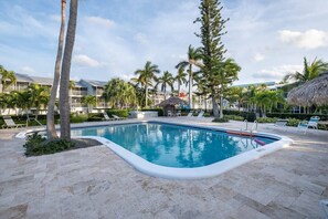A swimming pool surrounded by palm trees and lounge chairs, with a thatched-roof structure in the background. - Peekaboo View of Atlantic Ocean - Free Kayaks Pickleball (Key Largo)