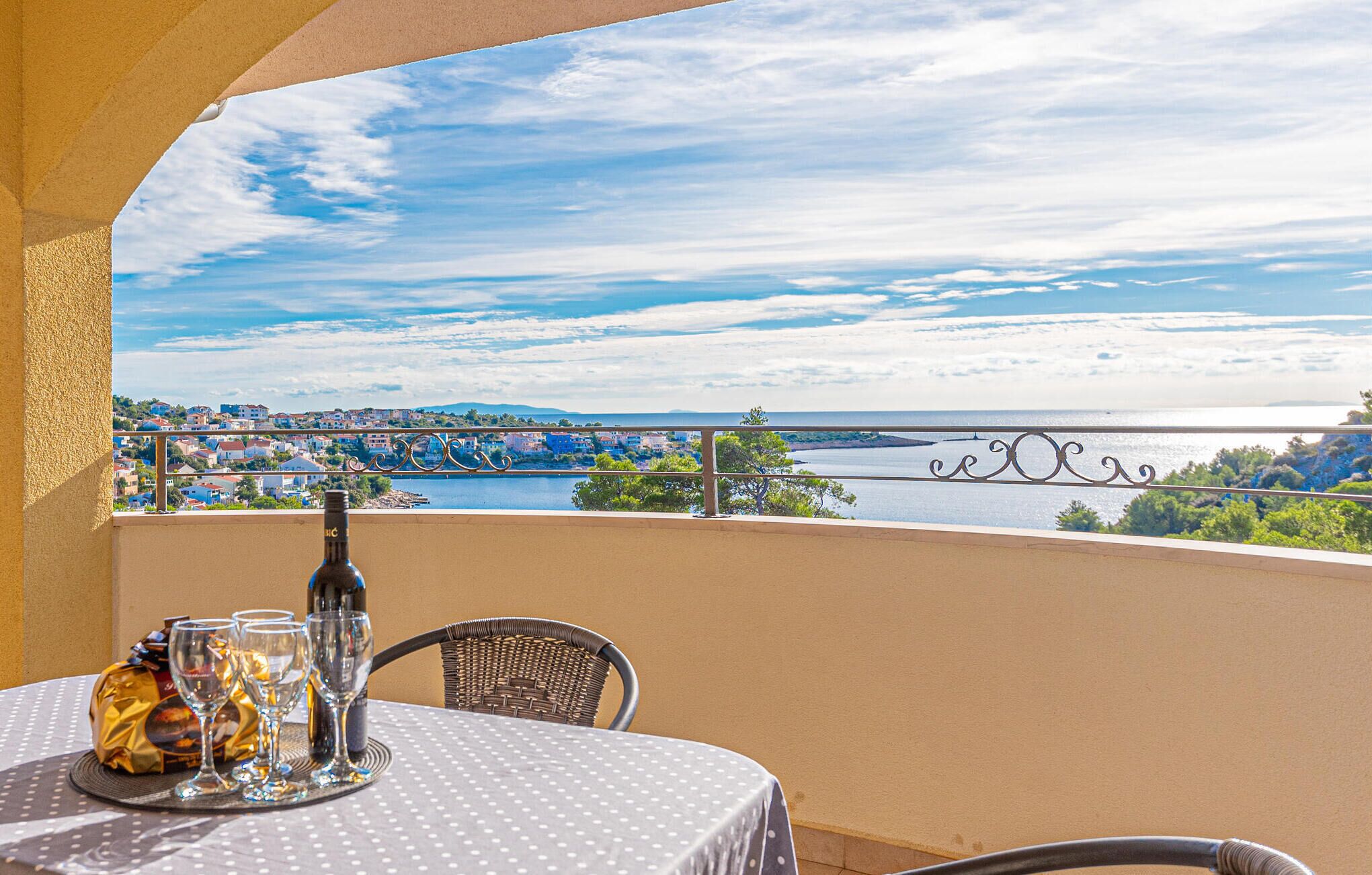 A balcony with a table set for two, overlooking a scenic view of a river and a bridge.